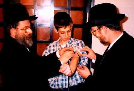 Bar mitzvah boy learning how to put on his new tefillin